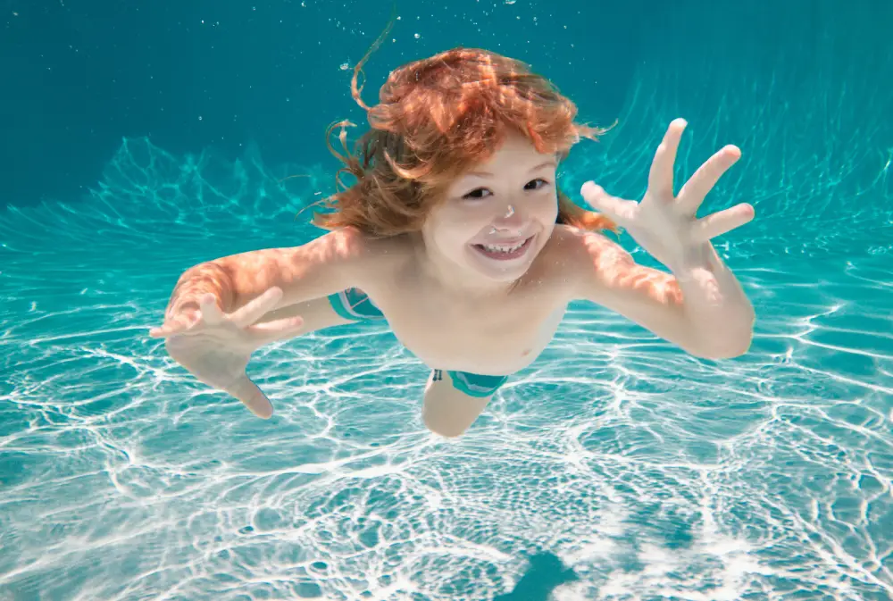 Kids Group Lessons (Ratio 1_4) Ages_ 3–13 Years Child underwater. Funny face portrait of child boy swimming and diving underwater with fun in pool.