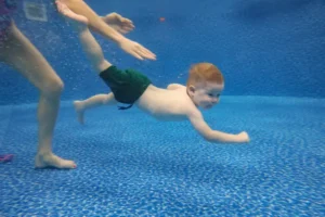 Baby boy dives underwater in the pool with pleasure
